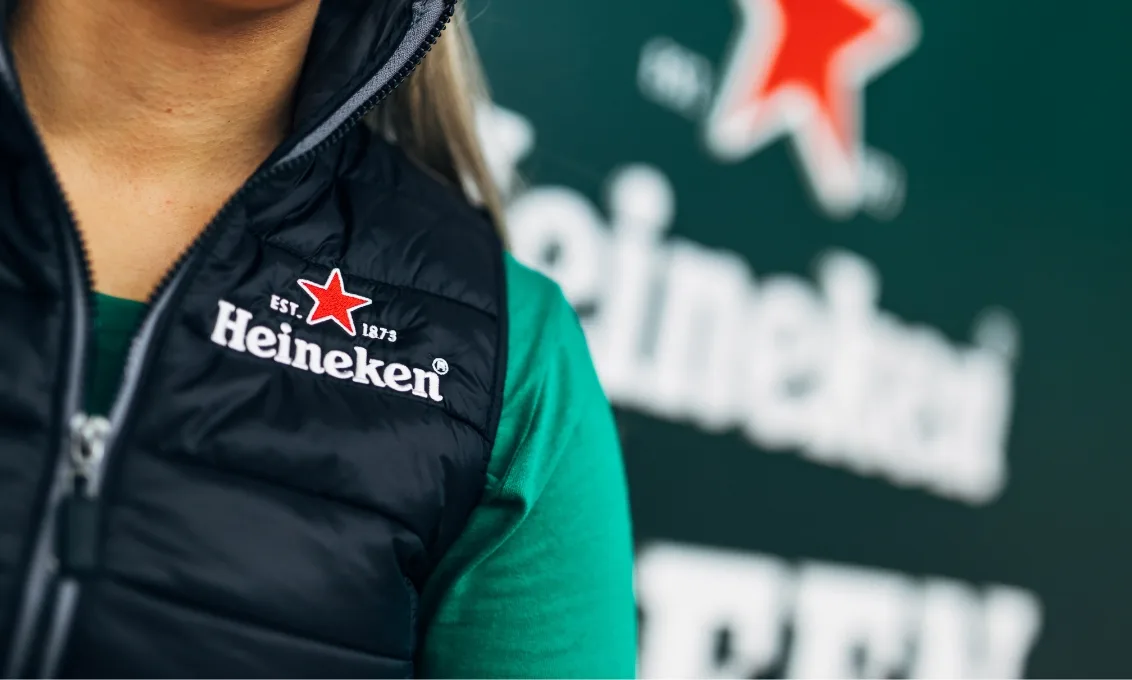 Close-up of a person wearing branded gilet with Heineken logo within the Heineken Lounge in The O2 Belfast.