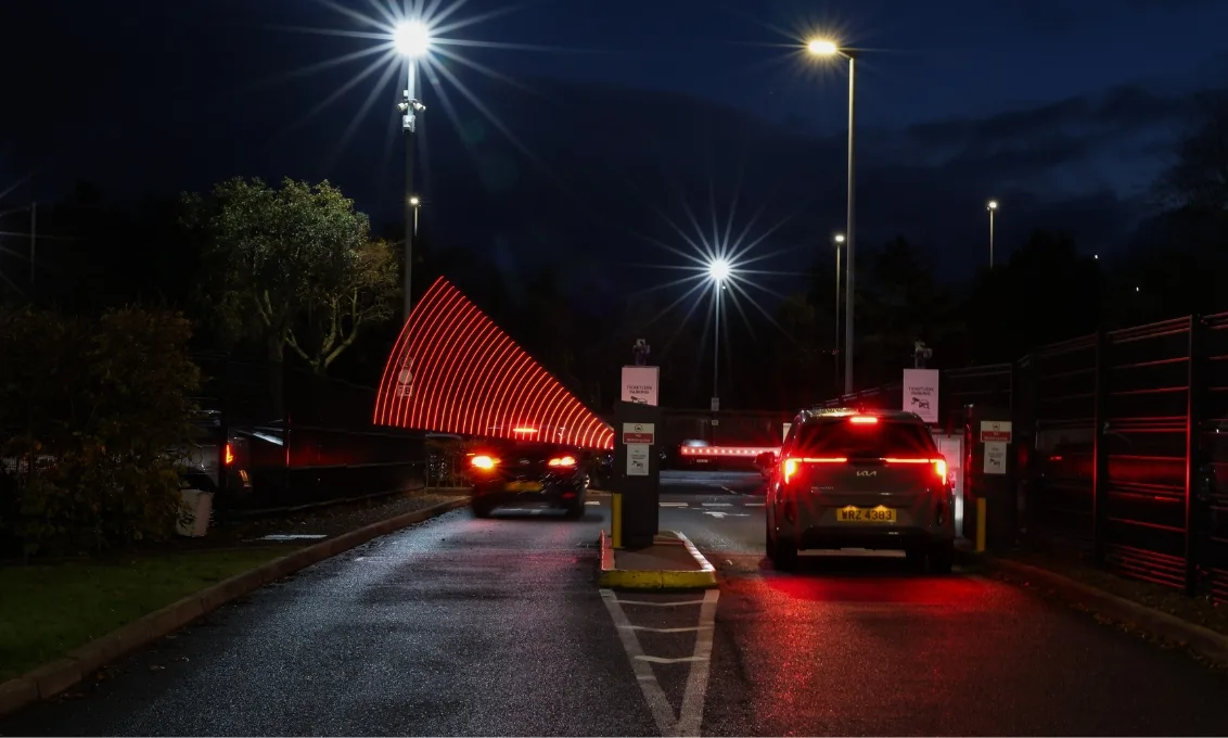 Car drives through open car park barrier as the other waits for barrier to lift.