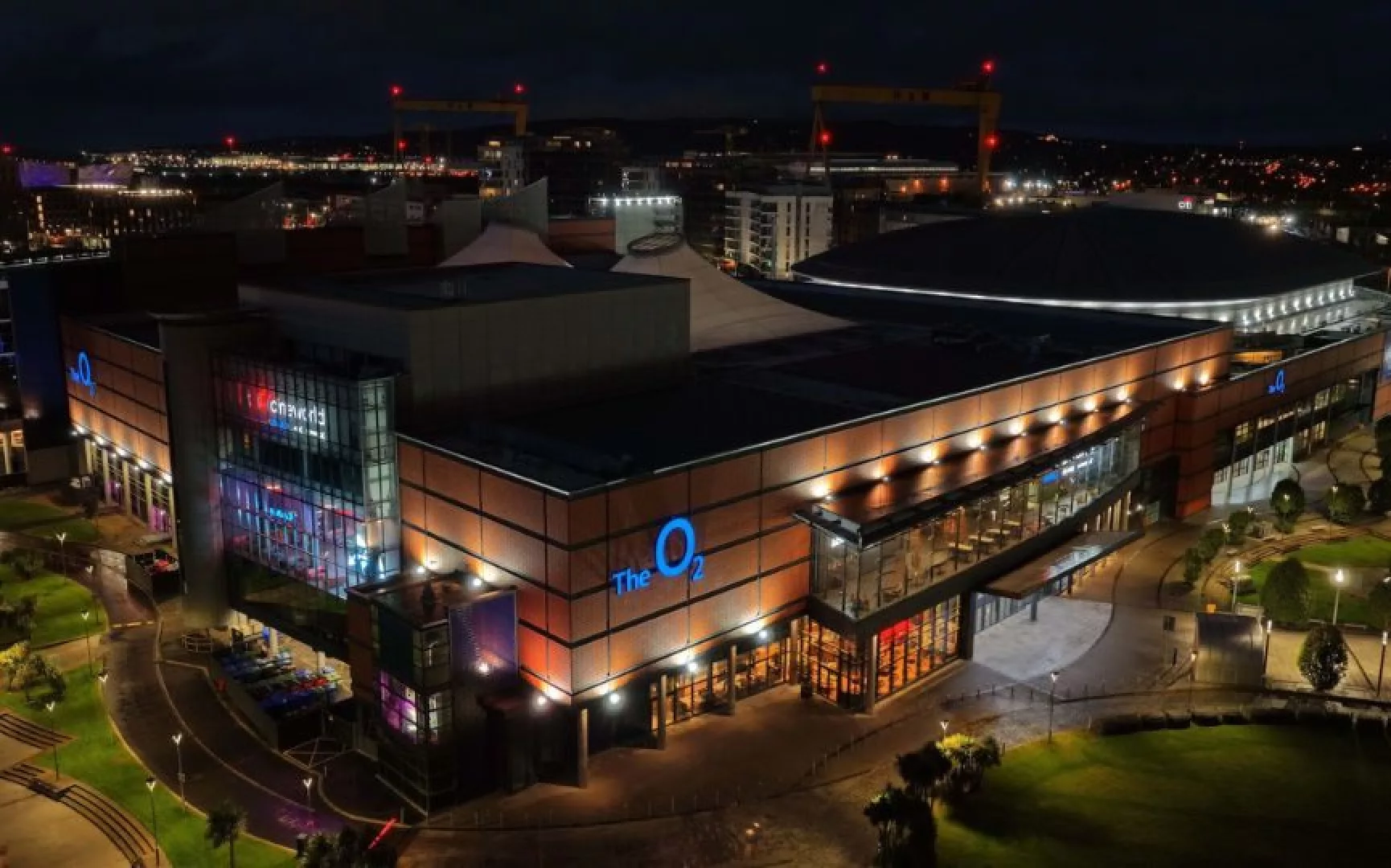 Aerial view of The O2 Belfast illuminated at night, highlighting the venue's modern exterior and surrounding cityscape.
