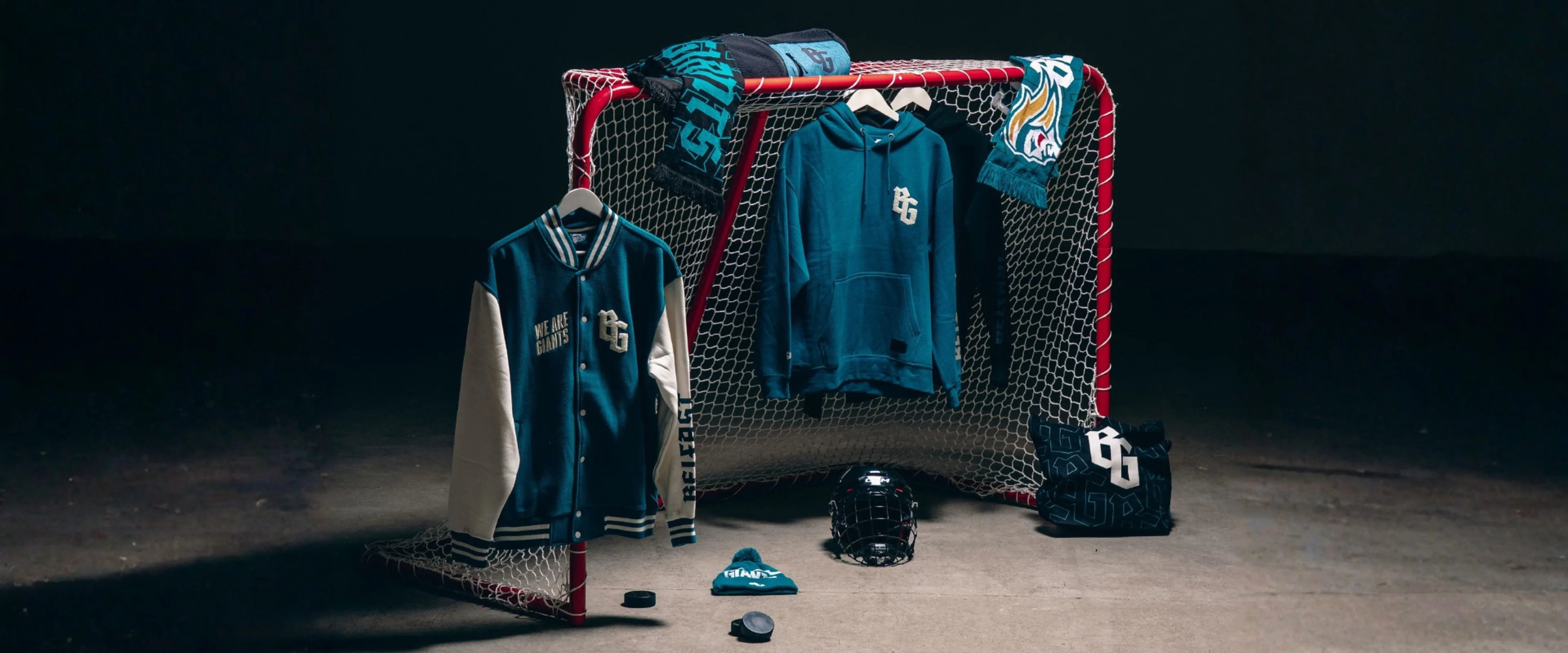 Belfast Giants merch is placed on a hockey net with a range of hoodies, hats and tote bags on display.